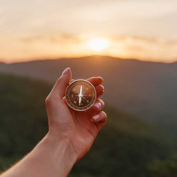 A hand holding a compass facing the sun indicating looking for purpose